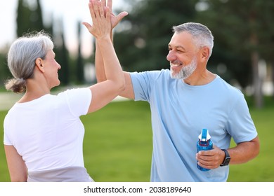 Senior couple family support in sports activities. Grey-haired spouses giving high five to each other with beaming smiles as sign of successful morning routine workout, jogging outside in city park - Powered by Shutterstock