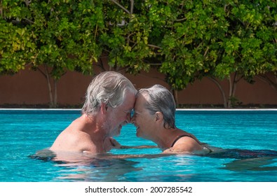 Senior Couple Floating In The Swimming Pool Water Head To Head, Happy Retirees Enjoying Summer Vacation