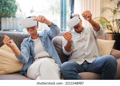 Senior Couple With Futuristic Virtual Reality Technology On The Sofa In Their Home. Retired Man And Woman Using Tech, Digital Gadgets And Vr Headset For 3d Games And Entertainment In The Metaverse