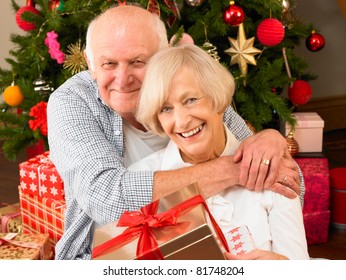 Senior couple with gifts in front of Christmas tree - Powered by Shutterstock