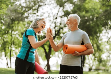 Senior couple is giving a high five after exercising together in the park on a sunny day, holding their orange yoga mats. Teamwork concept - Powered by Shutterstock