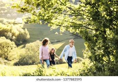 Senior Couple With Granddaughter On A Walk Outside In Spring Nature.