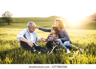 Senior Couple With Granddaughter Outside In Spring Nature At Sunset.