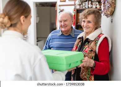Senior Couple Greeting Volunteer Woman Delivering A Hot Meal To Their Door