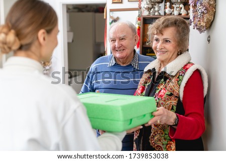 Senior couple greeting volunteer woman delivering a hot meal to their door