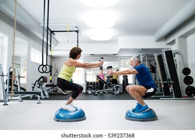 Senior Couple In Gym Working Out With Weights, Squatting