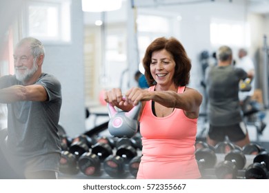 Senior Couple In Gym Working Out Using Kettlebells.