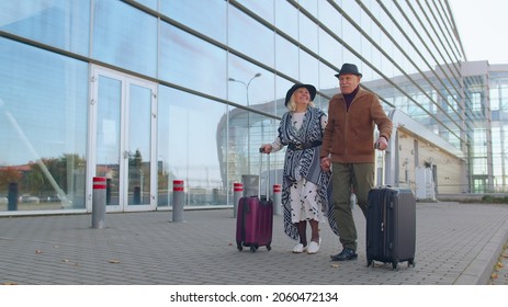 Senior couple happy pensioner tourists grandmother grandfather walking while carrying luggage suitcases on wheels from international airport hall or railway station. Travel, vacation, journey, trip