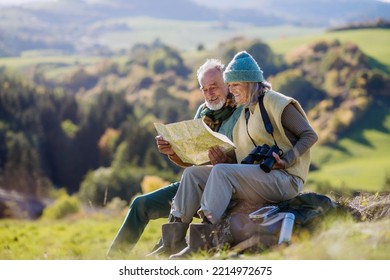 Senior couple having break, looking into paper map during hiking in autumn nature.