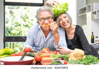 Senior Couple Having Fun In Kitchen With Healthy Food - Retired People Cooking Meal At Home With Man And Woman Preparing Lunch With Bio Vegetables - Happy Elderly Concept With Mature Funny Pensioner 