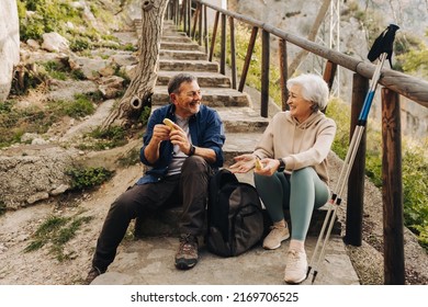 Senior Couple Having Some Bananas While Sitting At The Bottom Of A Hiking Trail. Happy Elderly Couple Taking A Break From Hiking. Mature Couple Spending Quality Time Together After Retirement.