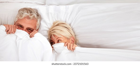 Senior couple, hiding and smile in bed for fun, comfort and bonding for love, silly and goofy together. Elderly people, marriage and sex in bedroom in retirement, romance and happiness at home