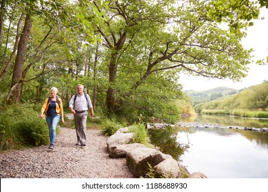 Senior Couple Hiking Along Path By River In UK Lake District