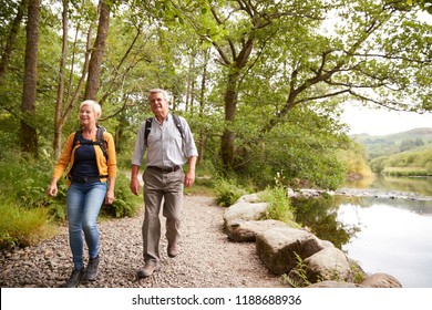 Senior Couple Hiking Along Path By River In UK Lake District