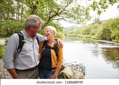 Senior Couple Hiking Along Path By River In UK Lake District