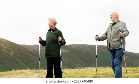 Senior couple hiking with poles in a scenic landscape. Seniors enjoying nature, hiking in the hills. Outdoor activity for elderly, exploring nature together. Senior couple hiking with sticks in nature - Powered by Shutterstock