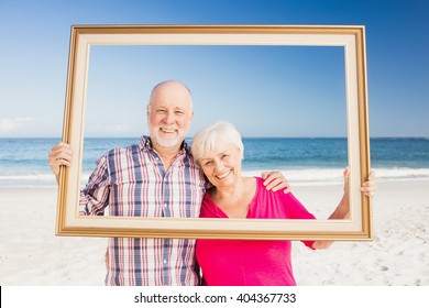 Senior couple holding frame at the beach - Powered by Shutterstock