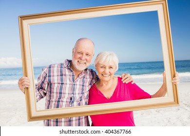 Senior couple holding frame at the beach - Powered by Shutterstock