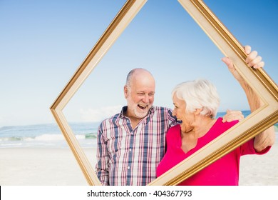 Senior couple holding frame at the beach - Powered by Shutterstock