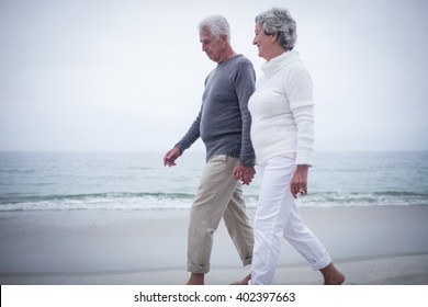 Senior couple holding hands and walking on the beach happily