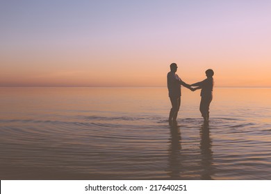 Senior couple holding hands in the water at sunset
