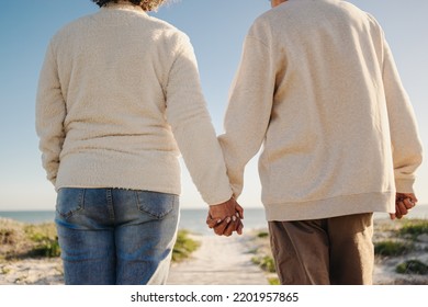 Senior couple holding hands while walking down a foot bridge at the beach. Unrecognisable elderly couple taking a refreshing seaside holiday after retirement. - Powered by Shutterstock