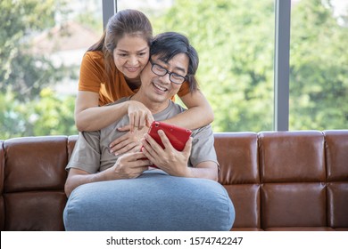 Senior Couple At Home , Enjoying Spending Time Together. Living Room Background. Generation Modern Technology Retirement Romantic Healthy Concept Asian Middle Age. Smiling Gesture Working With Laptop