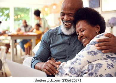 Senior Couple At Home Looking At Laptop Together With Multi-Generation Family In Background - Powered by Shutterstock