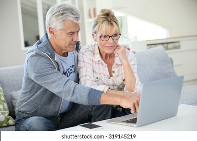 Senior Couple At Home Websurfing On Laptop Computer