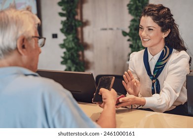 A senior couple at the hotel front desk makes contactless payments with a smartphone. Seniors traveling and using new technologies - Powered by Shutterstock