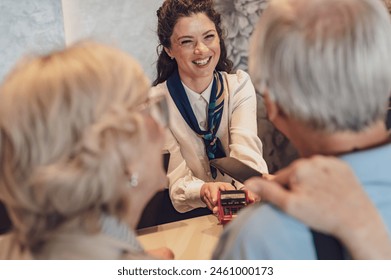 A senior couple at the hotel front desk makes contactless payments with a smartphone. Seniors traveling and using new technologies - Powered by Shutterstock