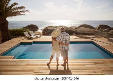 Senior couple hugging by modern pool overlooking ocean - Powered by Shutterstock