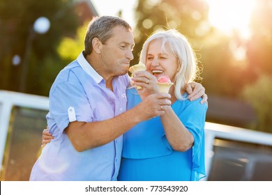 Senior Couple Hugging And Laughing Together, Eating Ice Cream. Mature Love.