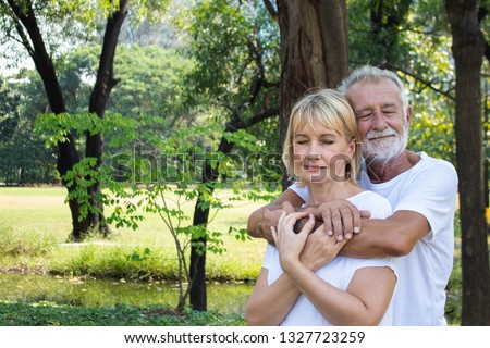 Senior couple hugging together. Close their eyes and feel deeply in love. they are in the park and wearing comfortable white shirt for summer.
