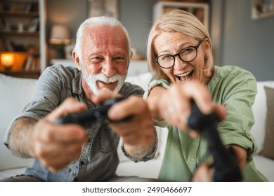 Senior couple husband and wife sit on sofa and play video games on joystick at home - Powered by Shutterstock