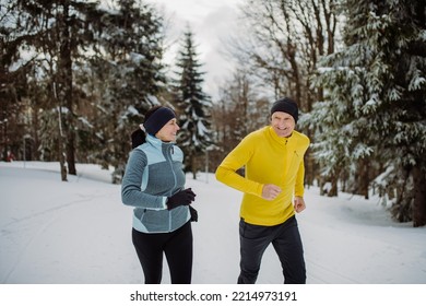 Senior Couple Jogging Together In Winter Forest.