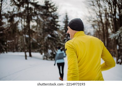 Senior Couple Jogging Together In Winter Forest.