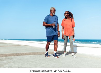 A senior couple joyfully walking together along a sunny beachside promenade, sharing laughter and good times in casual sporty attire. - Powered by Shutterstock