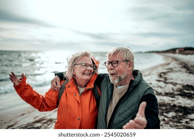 Senior couple laughing together on windy beach in raincoats - Powered by Shutterstock