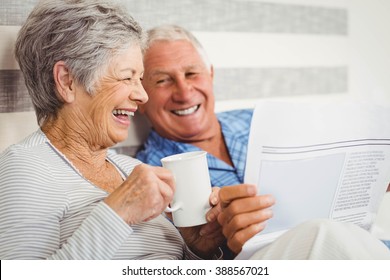 Senior couple laughing while reading newspaper in bedroom - Powered by Shutterstock