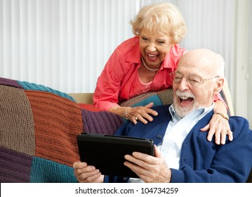 Senior Couple Laughing While Using Their Tablet Pc To Video Chat With Their Grandkids.