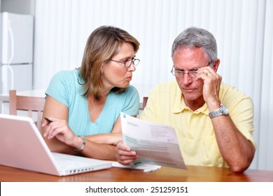 Senior Couple Looking Bills At Home With Computer.