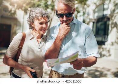 Senior Couple Looking At A Map While Sightseeing. Couple Of Mature Tourist Using City Map On Their Vacation.