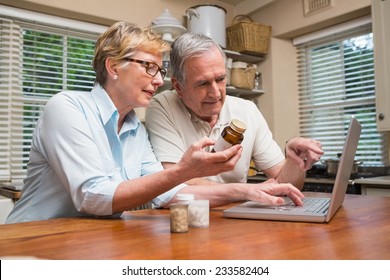 Senior Couple Looking Up Medication Online At Home In The Kitchen