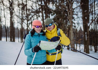 Senior Couple Looking At Paper Map During Cross Country Skiing In Snowy Forest.