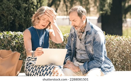 Senior couple looking sad and disappointed while using a laptop in a sunny park - Shutterstock ID 2288081501