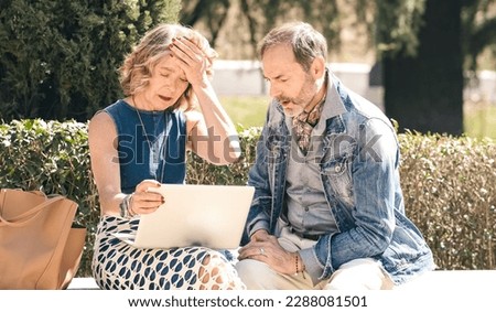 Senior couple looking sad and disappointed while using a laptop in a sunny park