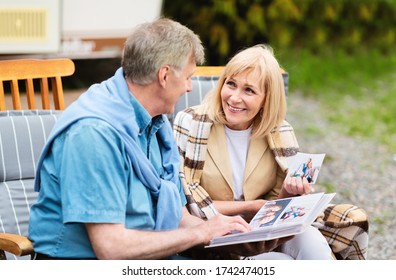 Senior Couple Looking Through Their Family Photo Album Near RV On Camping Site