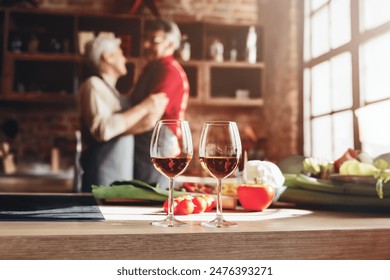 Senior couple in love dancing on their anniversary, celebrating with wine in kitchen, cooking, free space - Powered by Shutterstock