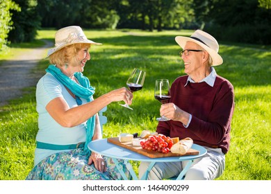 Senior couple in love picnicking in the park, sitting at a table, looking into each other's eyes, drinking wine, eating cheese with baguette and grapes. - Powered by Shutterstock